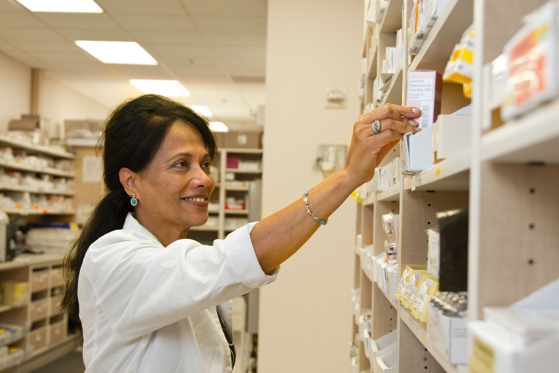 A pharmacist reaches up to get a medication off a shelf in a pharmacy