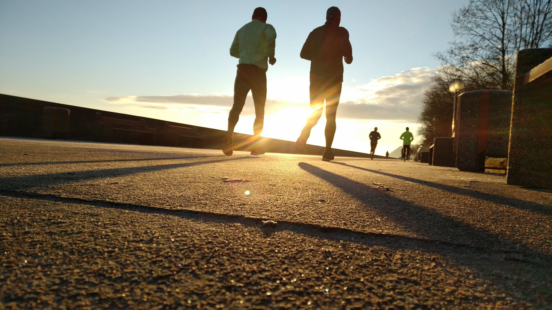 People running on a concrete path, silhouetted against the setting sun